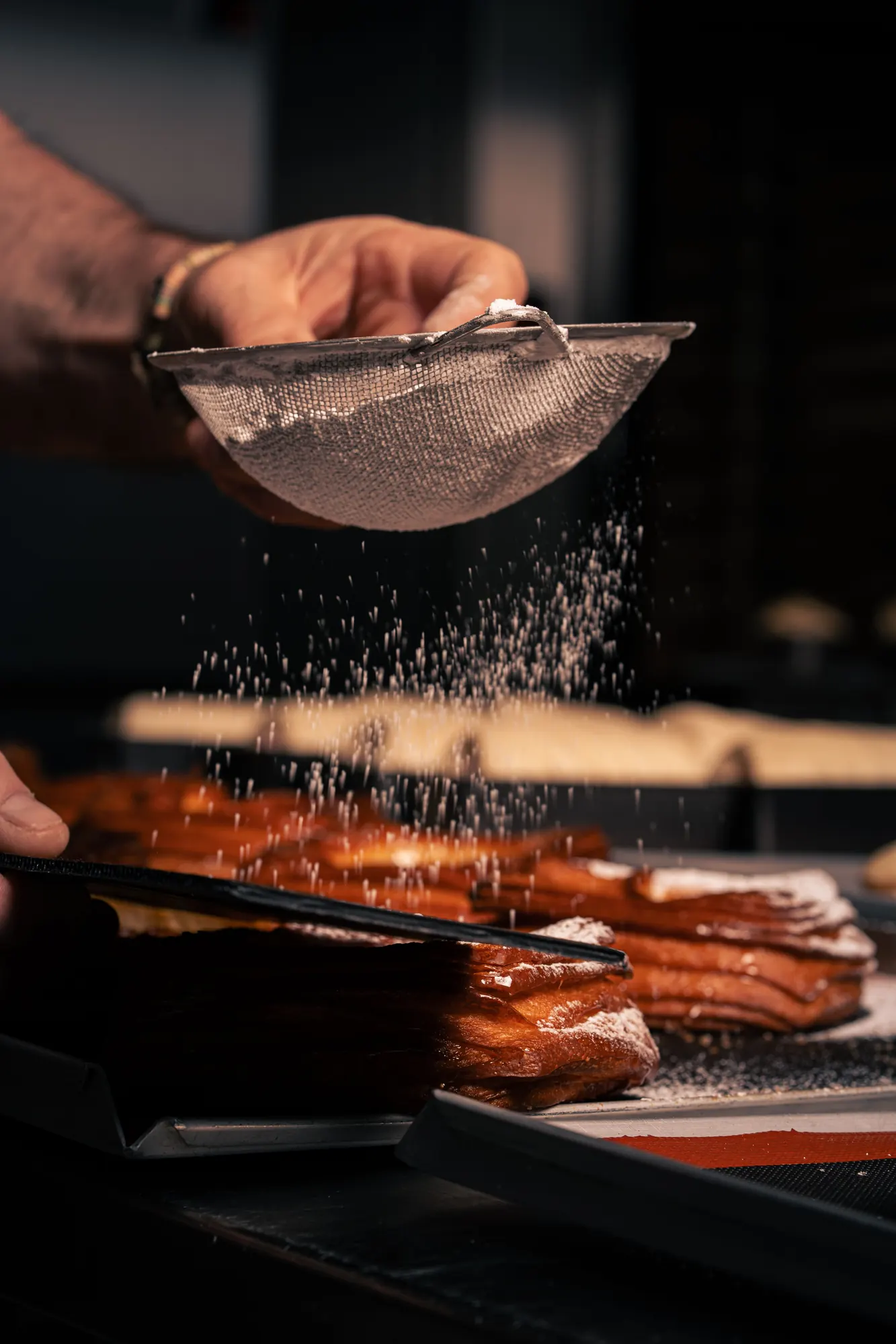 Icing sugar falling through a sieve over warm pastry